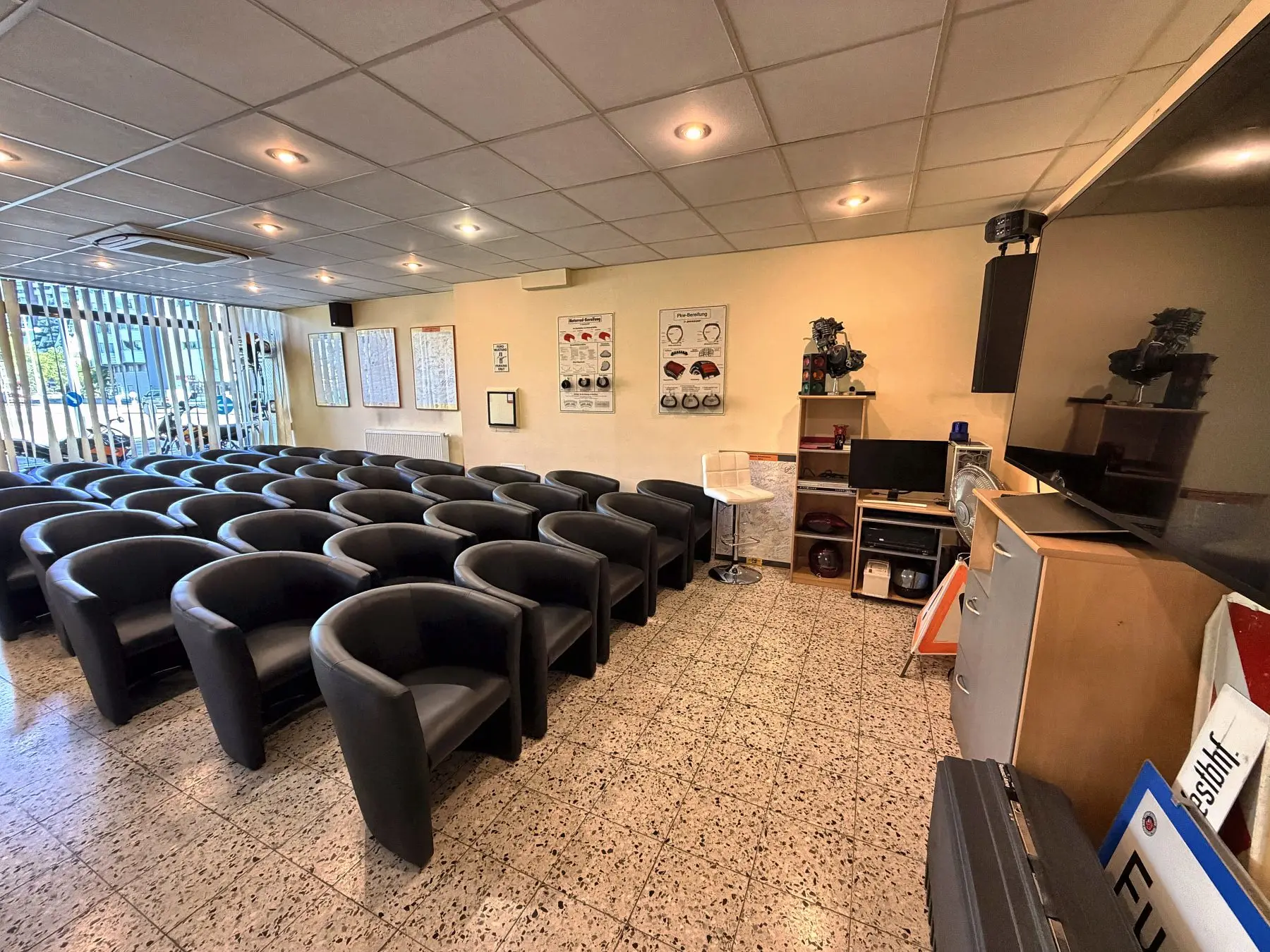 Kurssaal der Fahrschule Führerschein-Now mit Sitzreihen, grossem Bildschirm und Schautafeln zur Bereifung